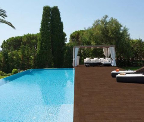 Piscina interrata con zona relax e area lounge in legno, immersa nel verde.