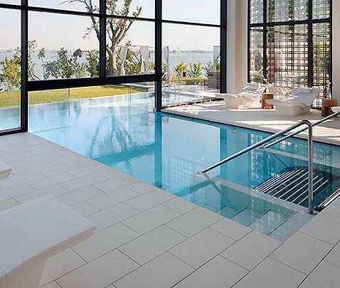 Piscina interrata con area wellness, grandi vetrate e vista panoramica, ambiente elegante e luminoso.