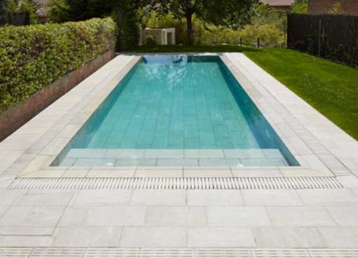 Piscina interrata con bordo a sfioro in giardino, immersa nel verde e con acque cristalline.