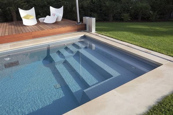 Piscina interrata a sfioro con scala a gradini, immersa in un giardino verde, ideale per relax e benessere all'aperto.