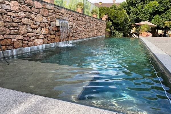Piscina a sfioro interrata con pareti in pietra e zona wellness all'aperto.