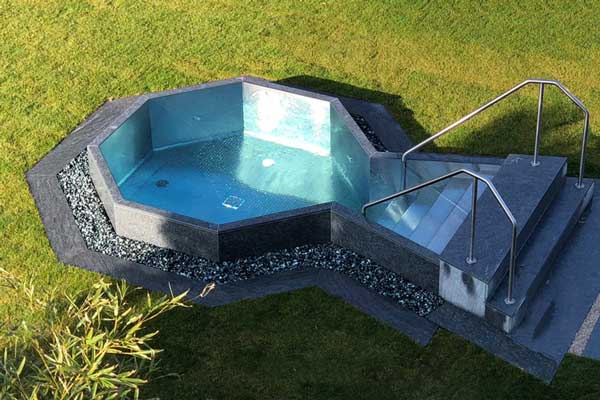 Piccola piscina interrata a sfioro con scala in acciaio, immersa nel verde giardino.