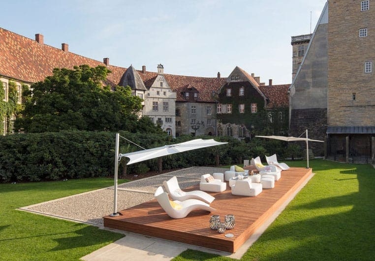 Relax spa area con chaise longue e ombrelloni sul prato verde in una corte storica, materiali moderni e colori neutri creano un ambiente accogliente e elegante.